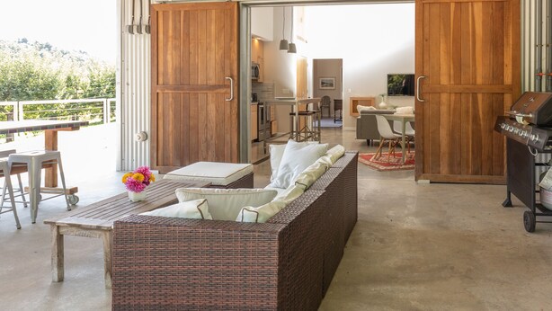 Un'area living esterna moderna con un divano in vimini, un tavolo da pranzo e un barbecue.