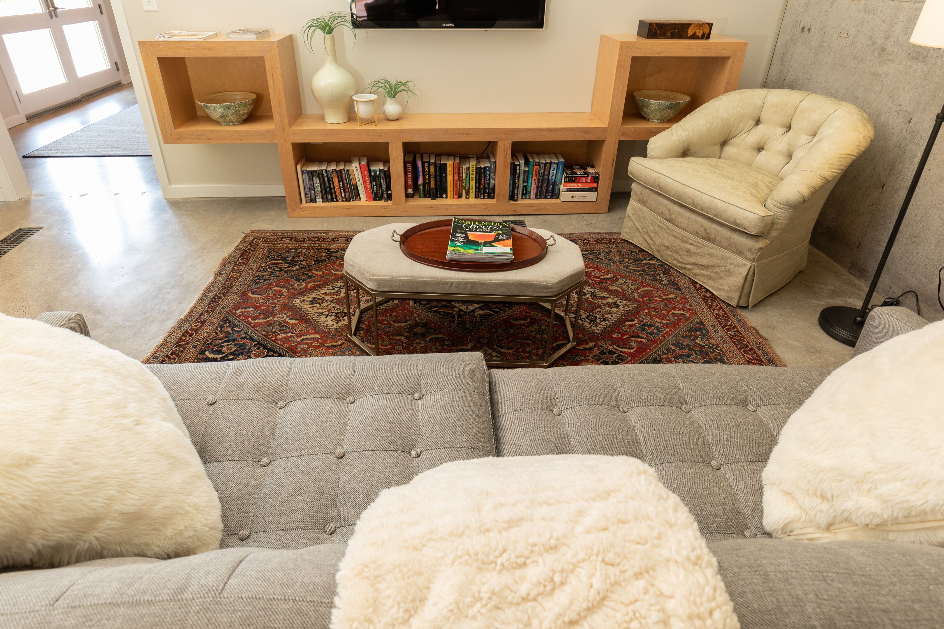 A living room with a sofa, armchair, ottoman, bookshelf, and a flat-screen TV.