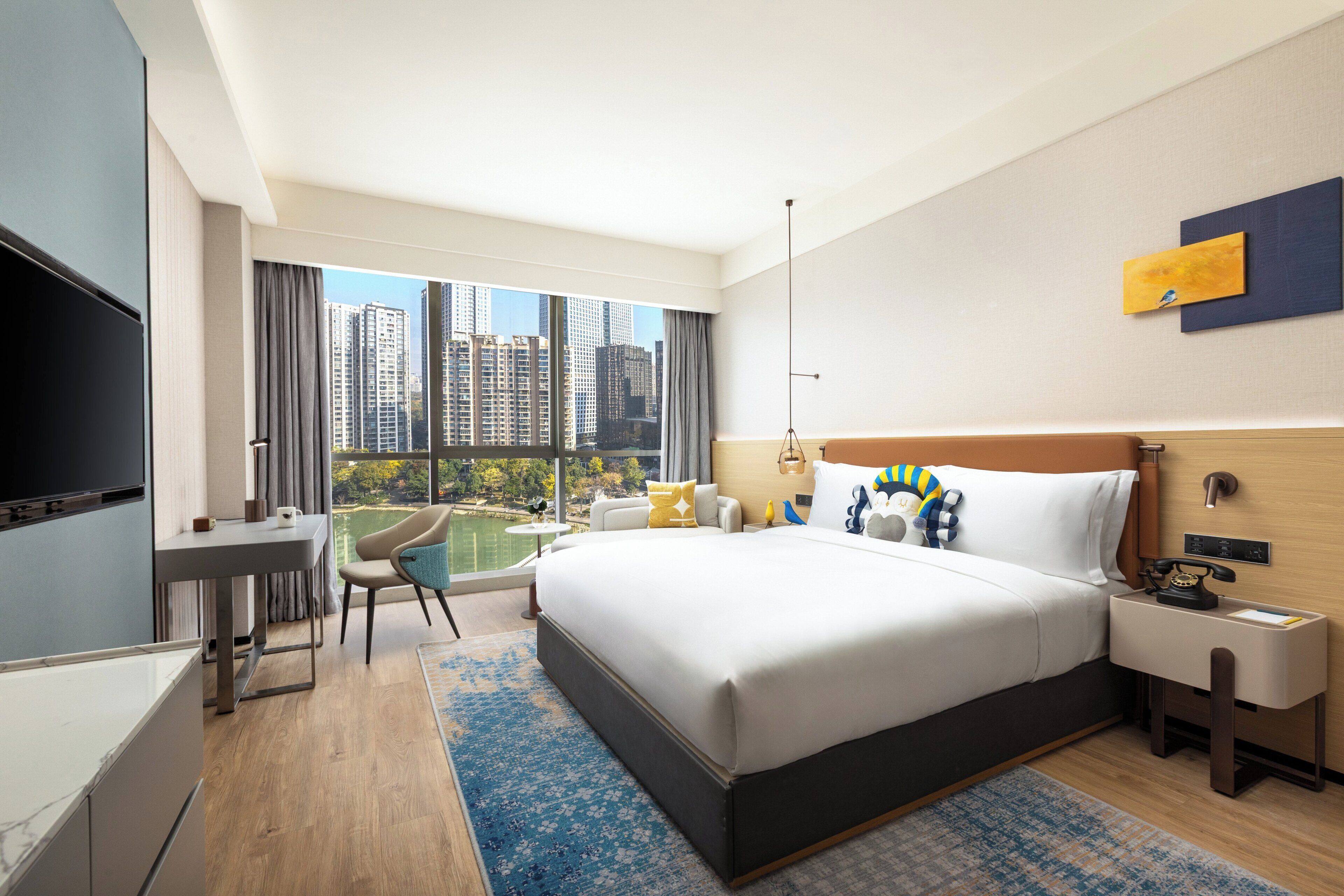 Ein modernes Hotelzimmer mit einem großen Bett, einem Schreibtisch, einem Sessel und einem Fernseher.