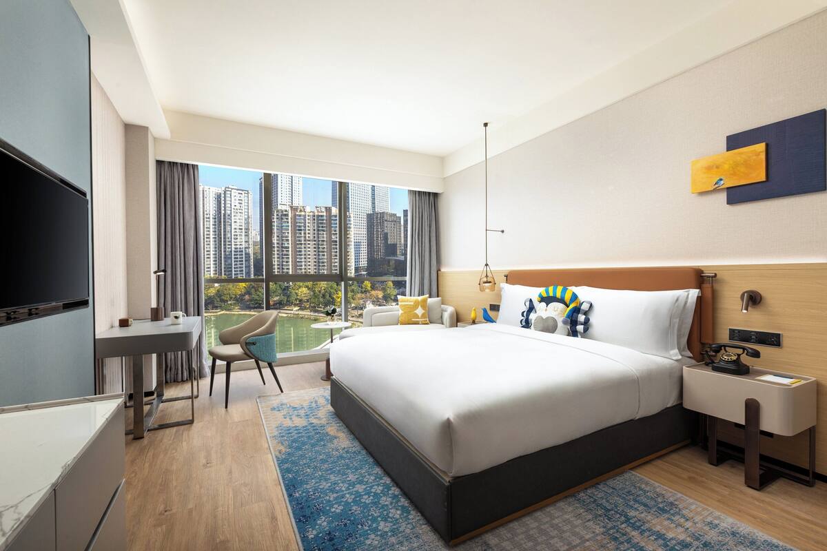 A modern hotel room with a large bed, a desk, a chair, and a TV.