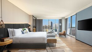 A modern hotel room with a large bed, a sofa, a TV, and a city view.