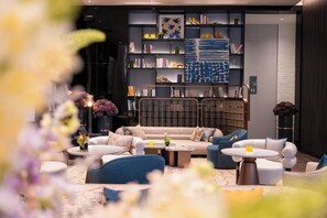 Ein moderner Loungebereich mit einer Couch, Sesseln und einem Couchtisch. Ein Bücherregal beherbergt Bücher und Dekorationselemente.
