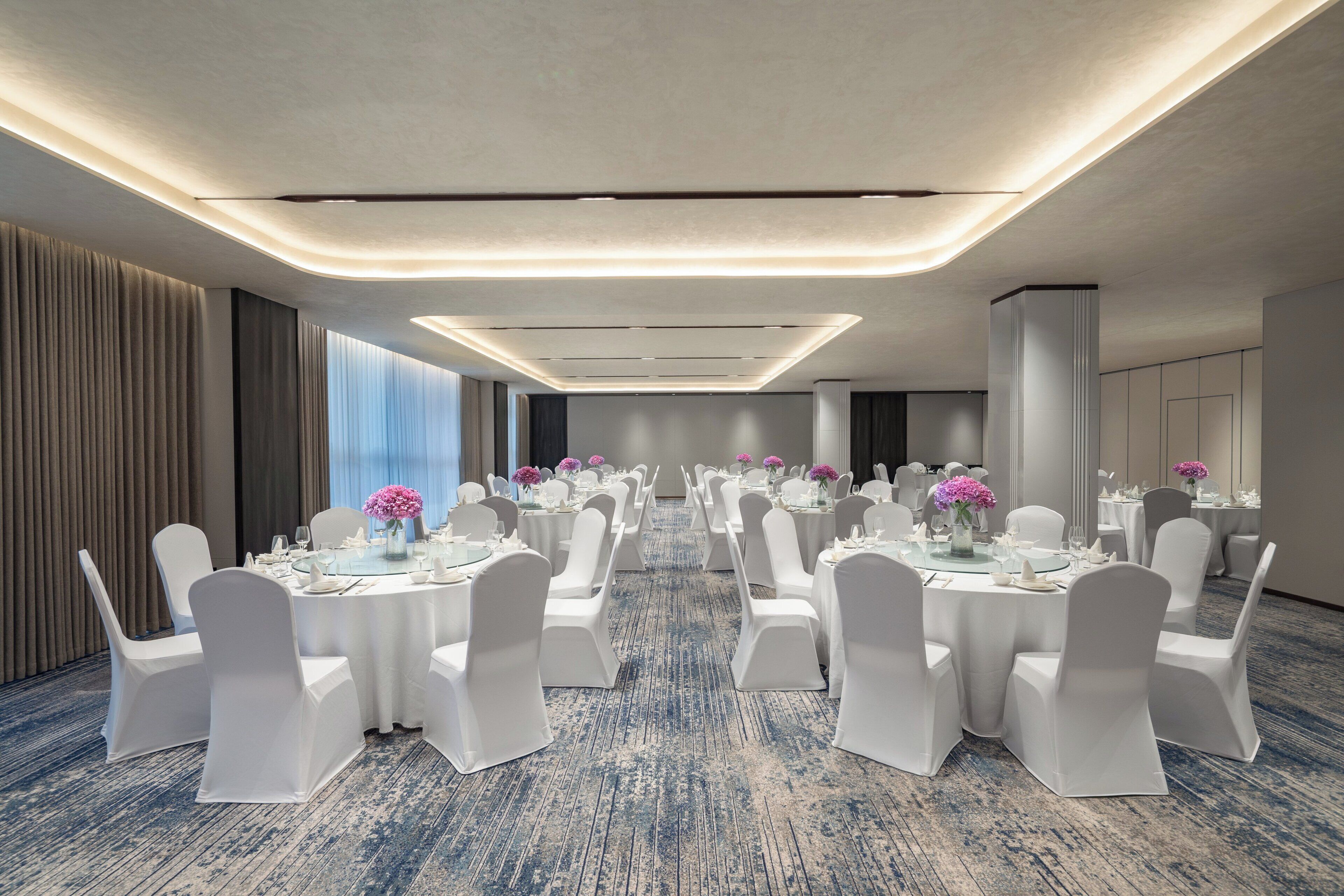 A conference room with round tables, white chairs, and floral centerpieces.
