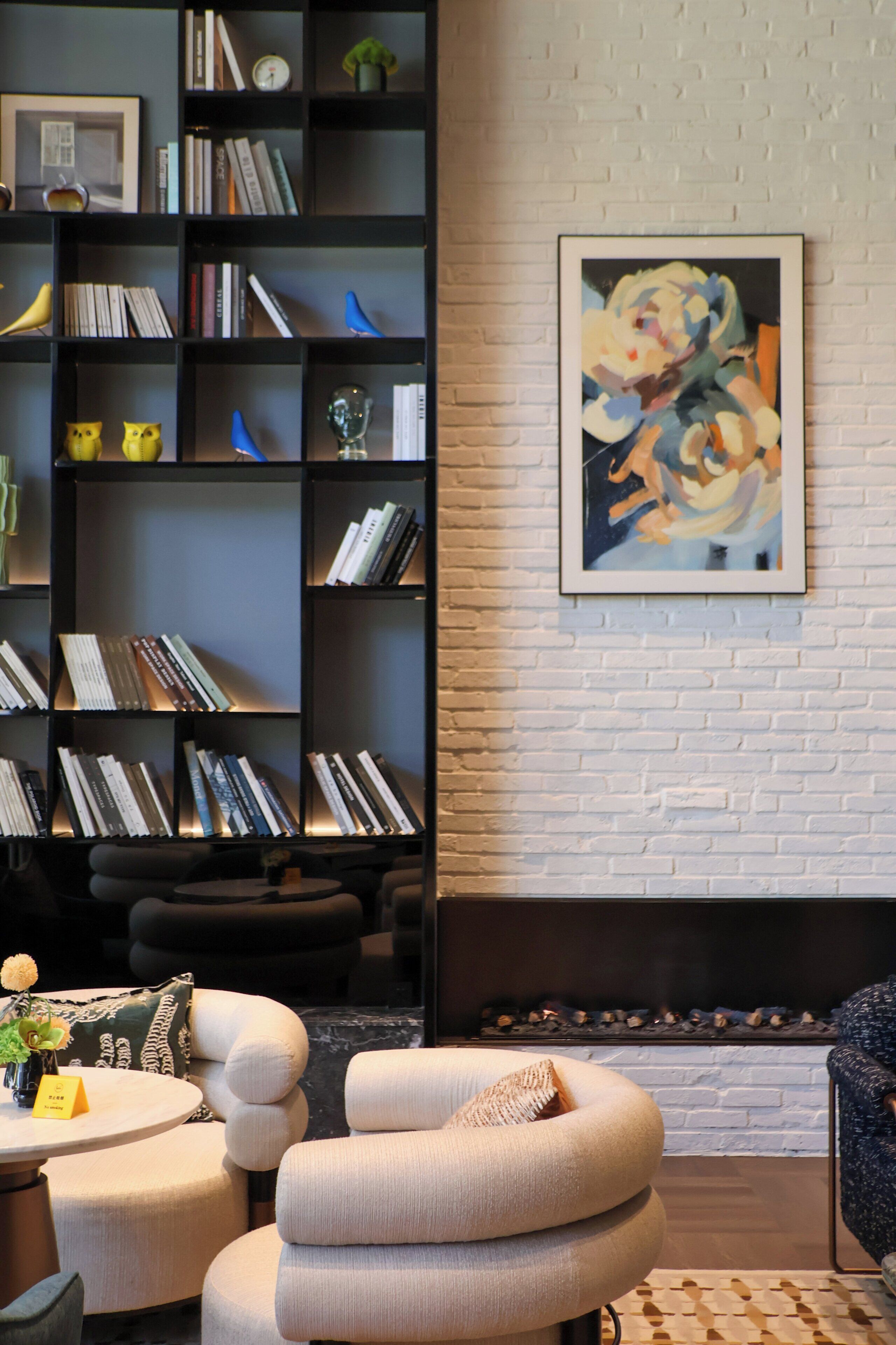 A modern living room with a fireplace, a bookshelf filled with books, and a large abstract painting on the wall.