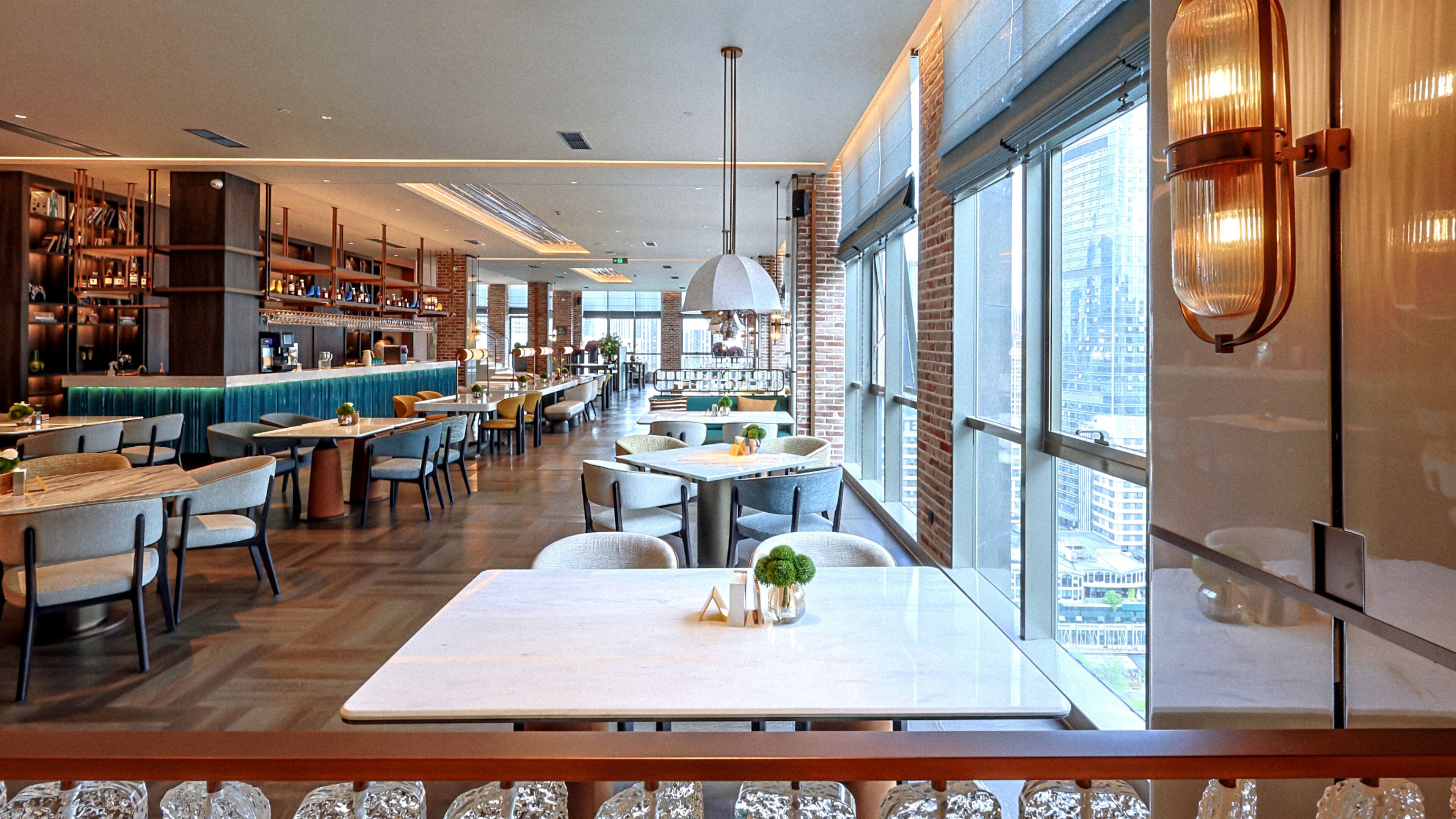 Een modern restaurant met een bar, zitplaatsen en grote ramen met uitzicht op de stad.