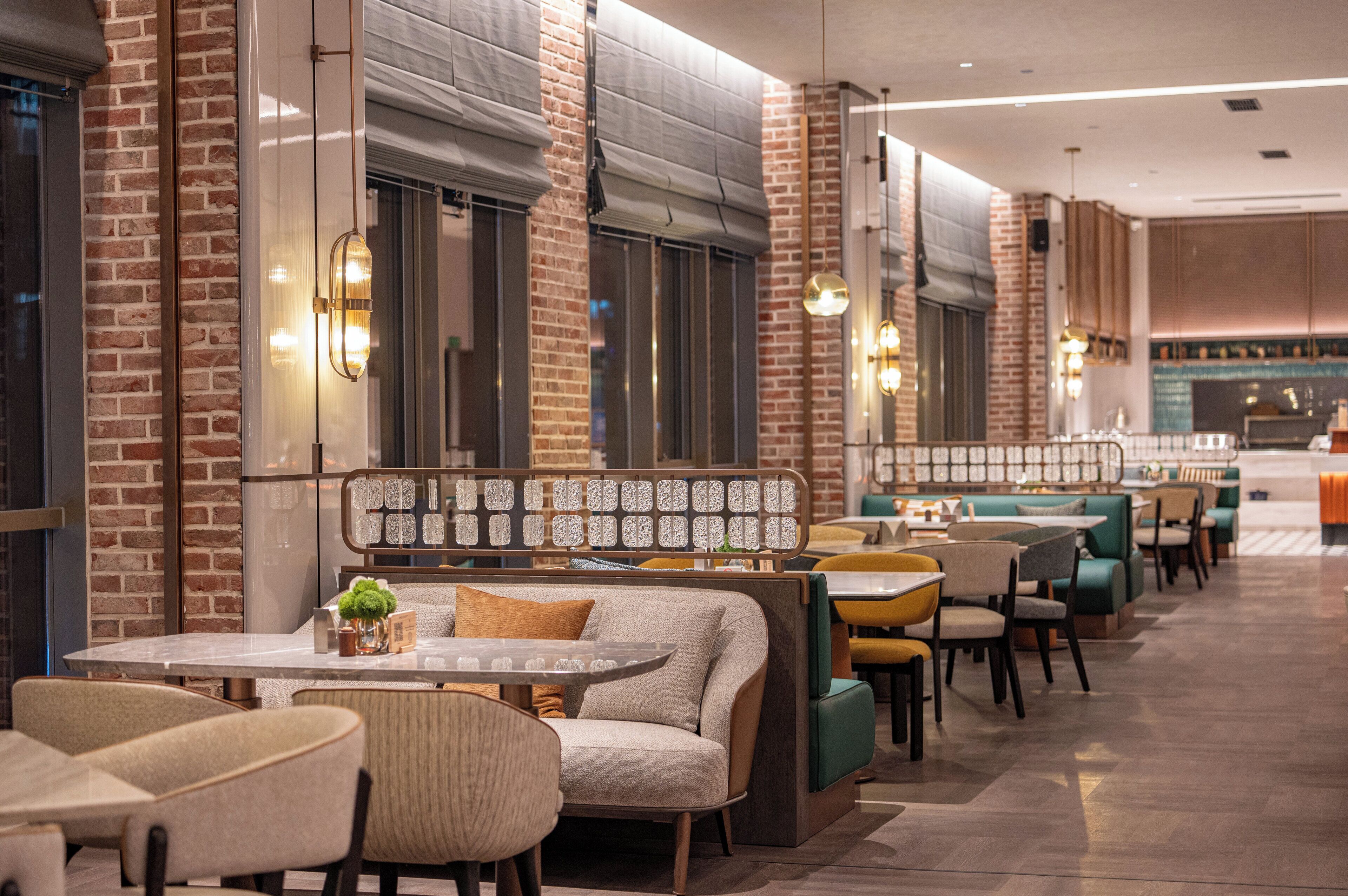A restaurant interior with brick walls, cushioned seating, and pendant lighting.