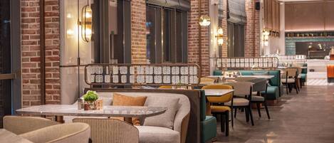 A restaurant interior with brick walls, cushioned seating, and pendant lighting.