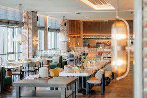 Ein Restaurant mit mehreren Tischen und Stühlen, großen Fenstern und einer Ziegelwand.