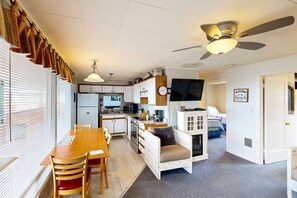 Cozy living space with kitchenette, dining area, and seating area, featuring a ceiling fan, TV, and welcoming sign.
