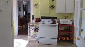 A kitchen with a white stove, a red kettle, and a microwave on a red shelf. There is a white cabinet above the stove and a door leading to another room. - Water front property with spectacular views.  (Marrowstone)