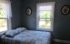 Un dormitorio con cama, dos ventanas y decoraciones florales en las paredes.