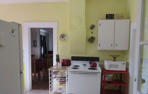 Una cocina con una estufa blanca, un hervidor rojo y un microondas sobre un estante rojo. Hay un armario blanco sobre la estufa y una puerta que da a otra habitación.