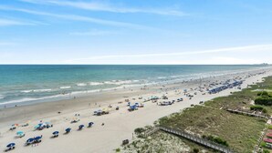 A beach with rows of umbrellas and beach chairs, a wooden boardwalk, and a clear view of the ocean. - 9th Floor Oceanfront Condo, Jacuzzi Tub, Outdoor Pool | Ocean Bay Club - 906 (North Myrtle Beach)