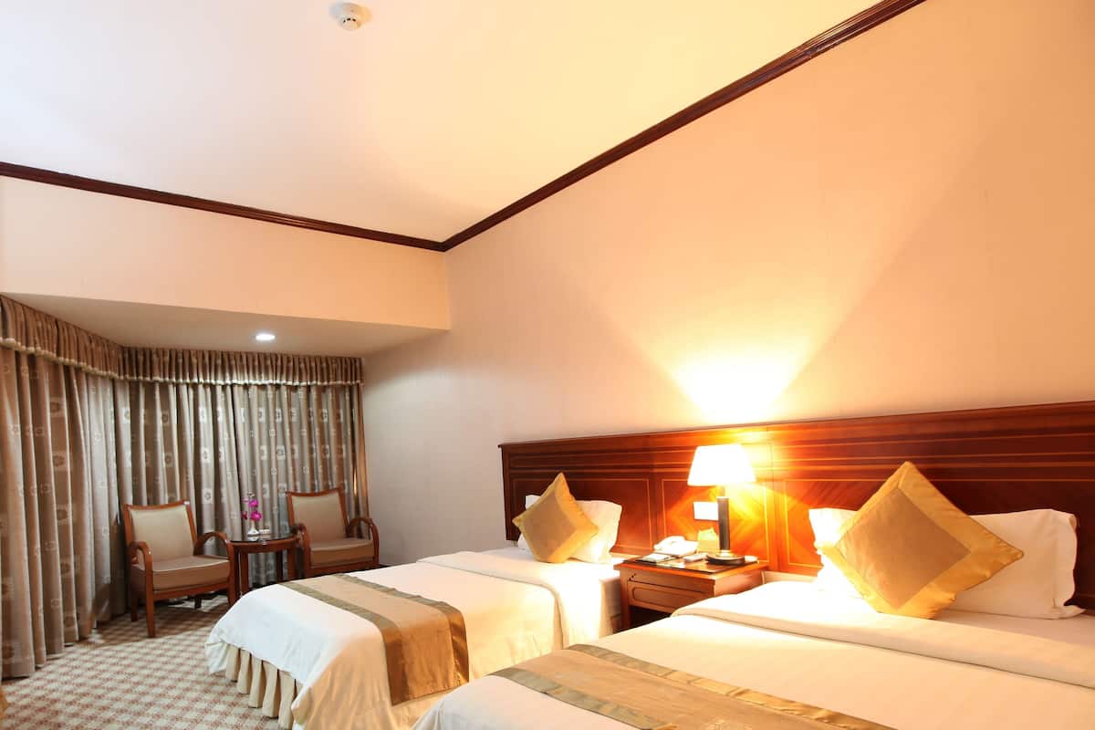 Quarto de hotel com duas camas, uma escrivaninha, uma cadeira e um abajur.