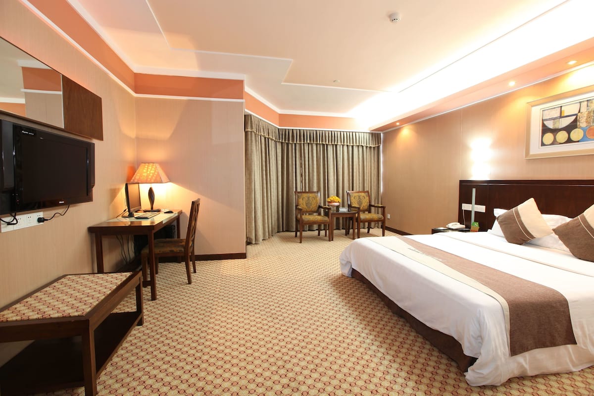 Quarto de hotel com cama, escrivaninha, cadeiras e televisão.