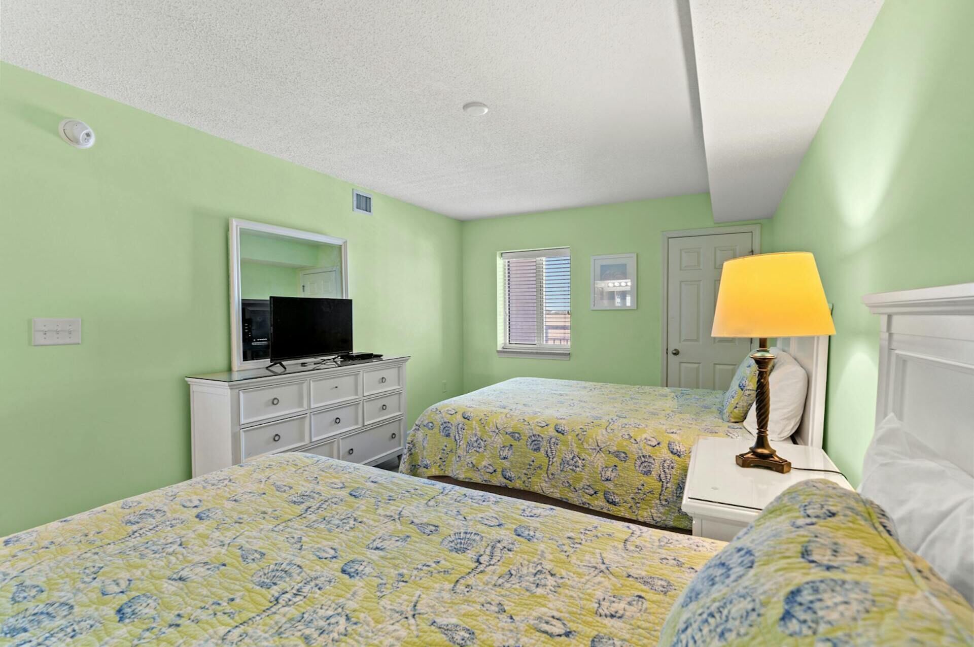 Une chambre avec deux lits, une commode, un téléviseur et une lampe.
