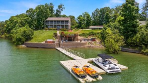 A lakeside property with a dock, two jet skis, a covered seating area, and a house with a deck. - Best Lakefront Views, NEW Hot Tub, FirePit, Dock, Kayaks, Dog Friendly (Dandridge)