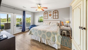 A bedroom with a large bed, a ceiling fan, a view of the outdoors, and a small table with a lamp. - Best Lakefront Views, NEW Hot Tub, FirePit, Dock, Kayaks, Dog Friendly (Dandridge)