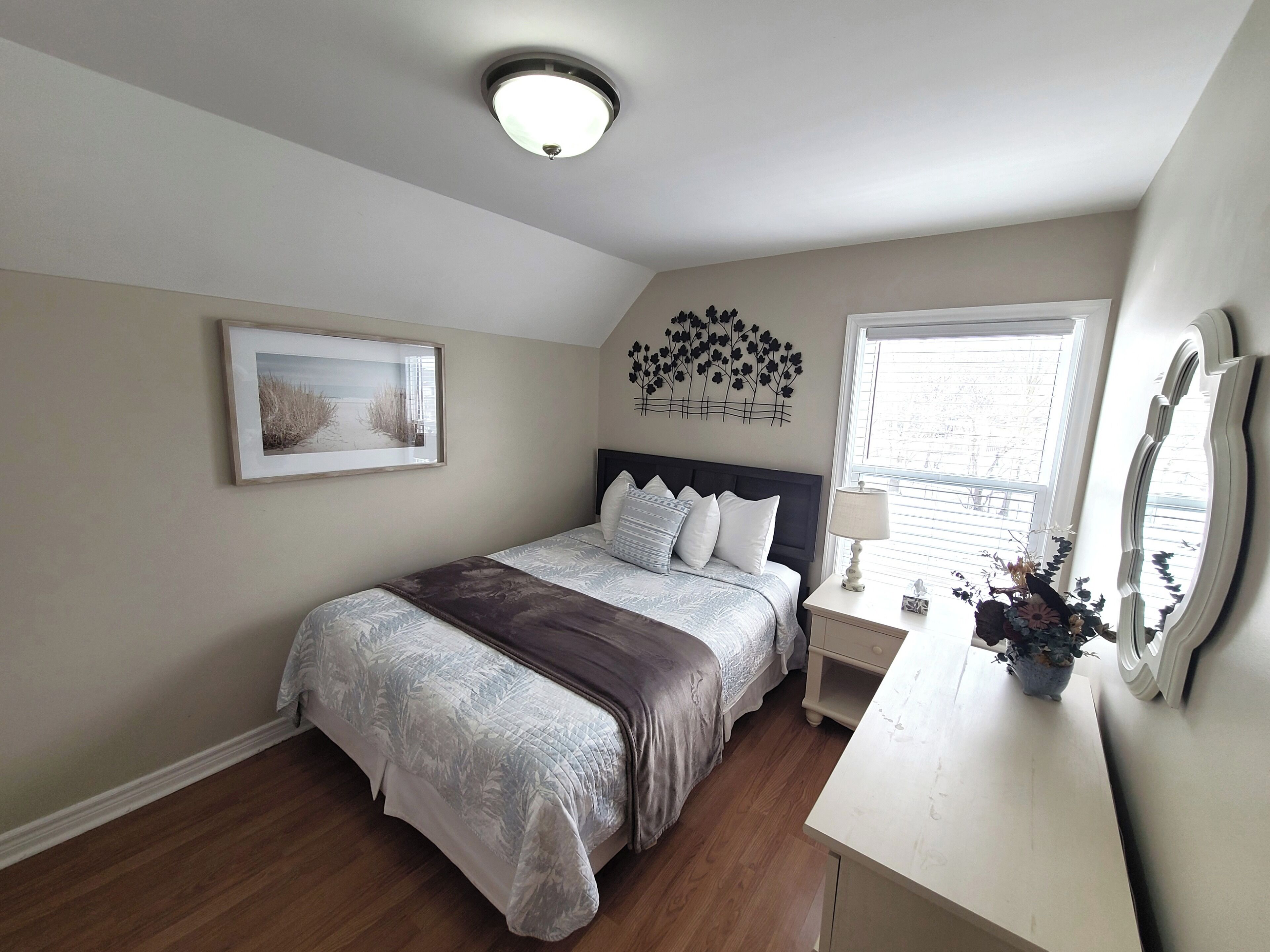 A bedroom with a bed, bedside table, lamp, and a window with blinds.