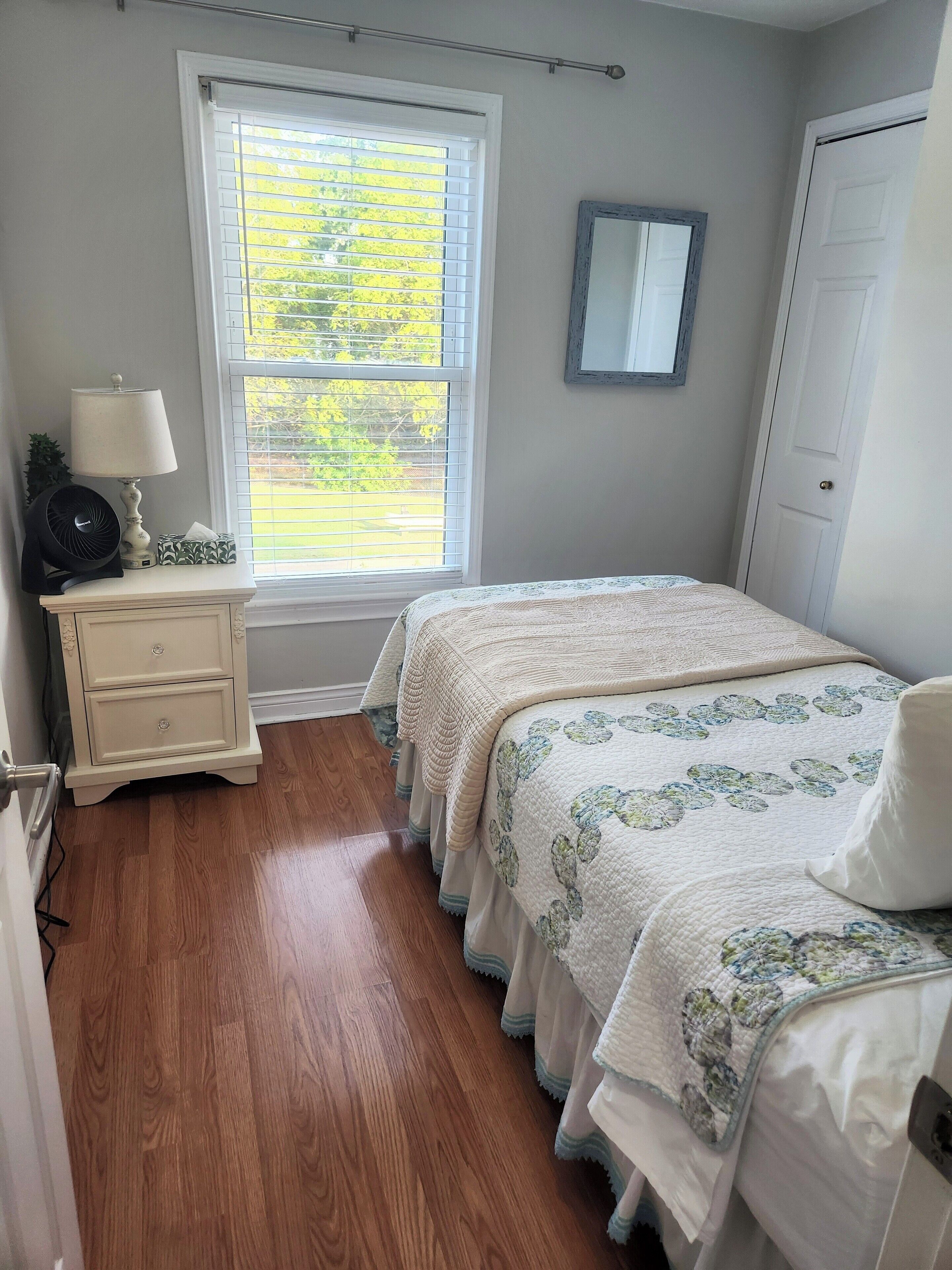 Un dormitorio con cama, mesita de noche, ventana y puerta.