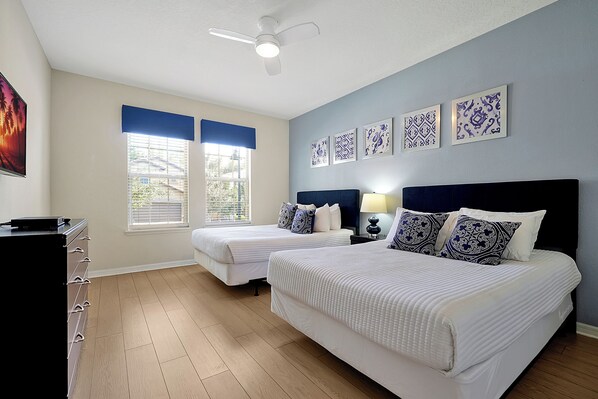 A hotel room with two beds, a ceiling fan, and artwork on the wall.