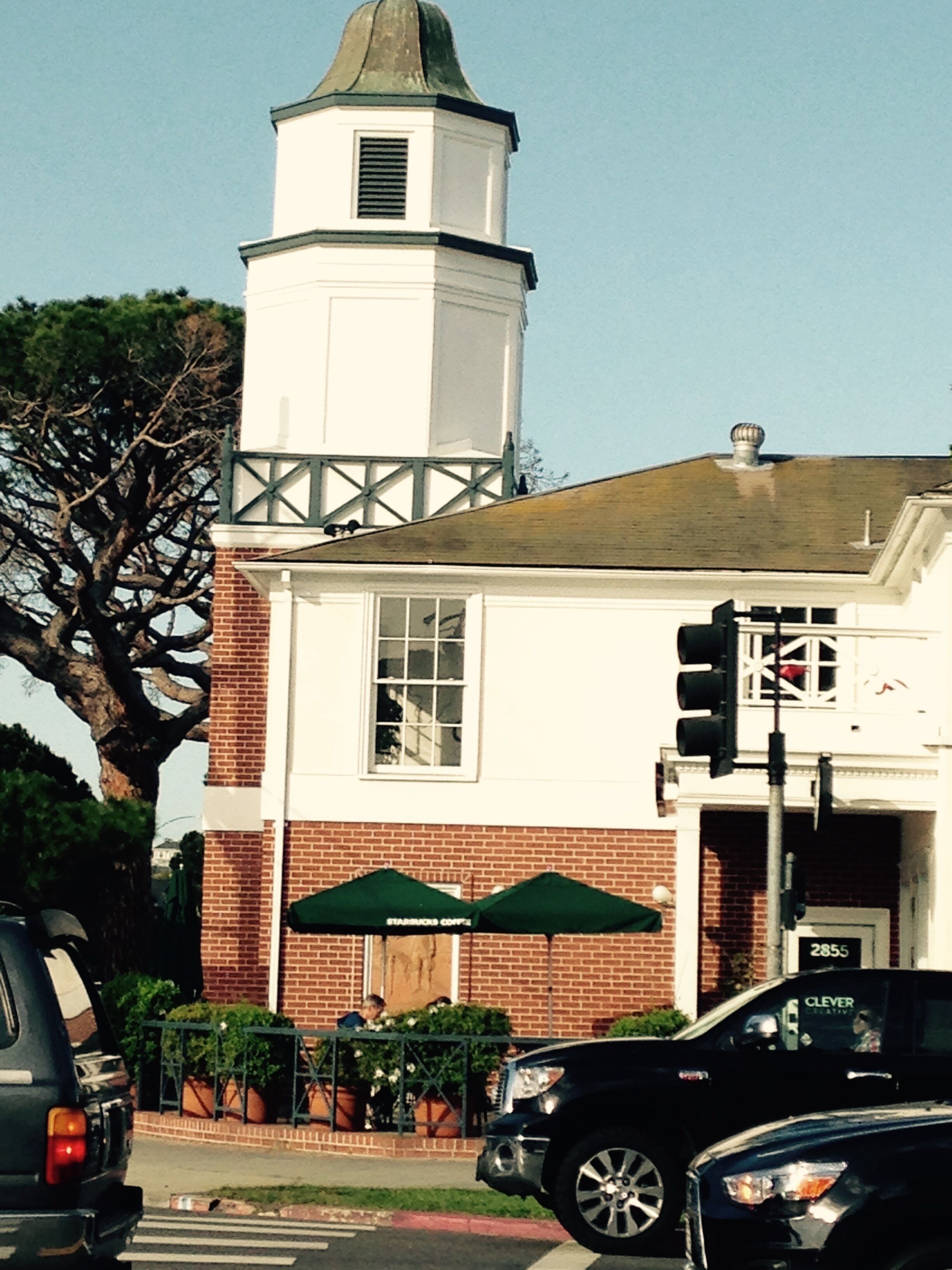 A building with a white tower, brick facade, and green umbrellas.