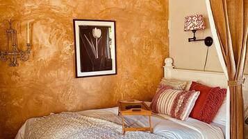 A bed with a wooden tray, a framed picture, a wall-mounted lamp, and a curtain.