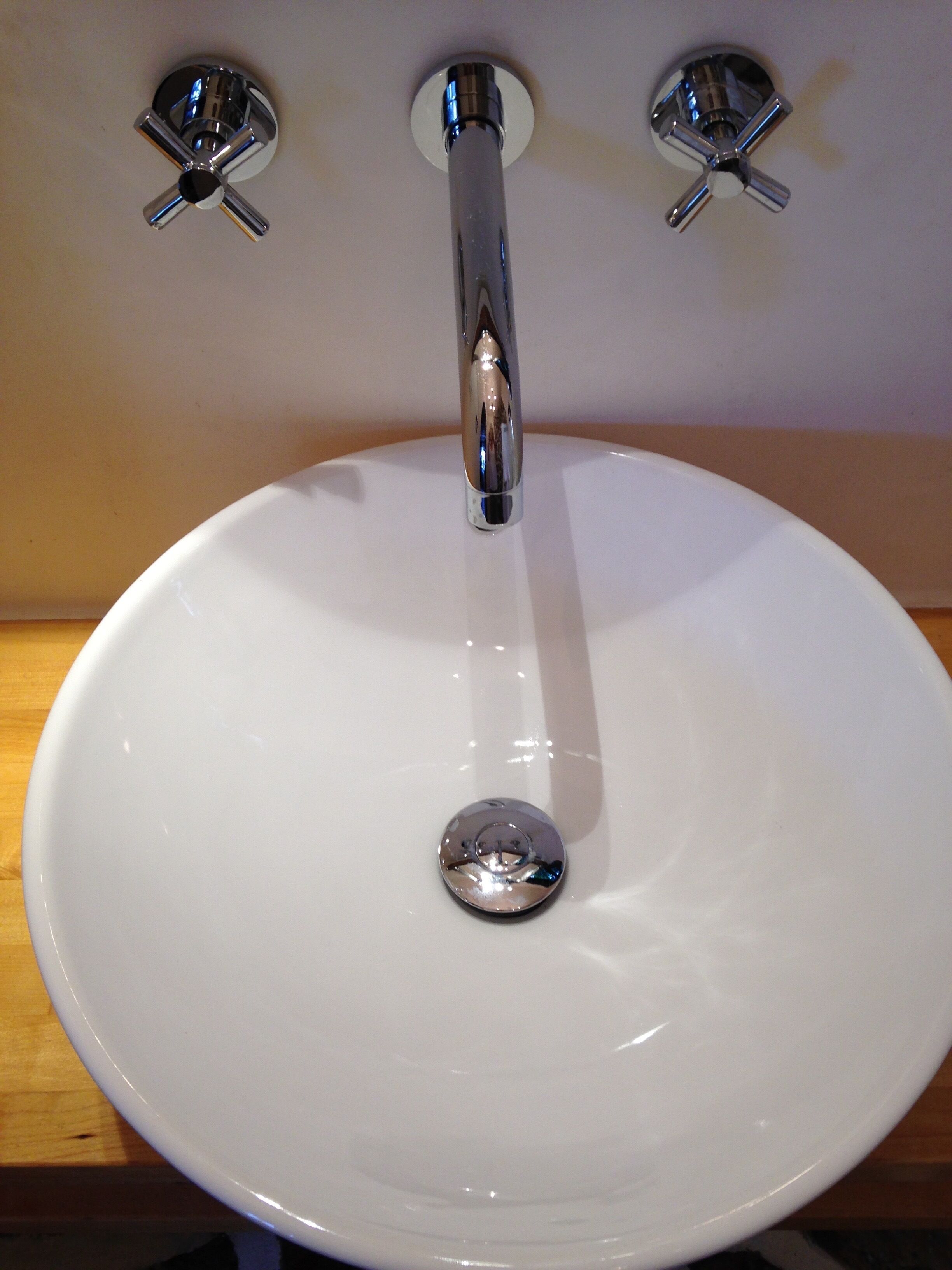 A white ceramic sink with a chrome faucet and three chrome handles on the wall.