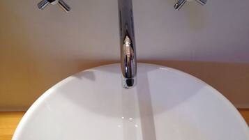 A white ceramic sink with a chrome faucet and three chrome handles on the wall.
