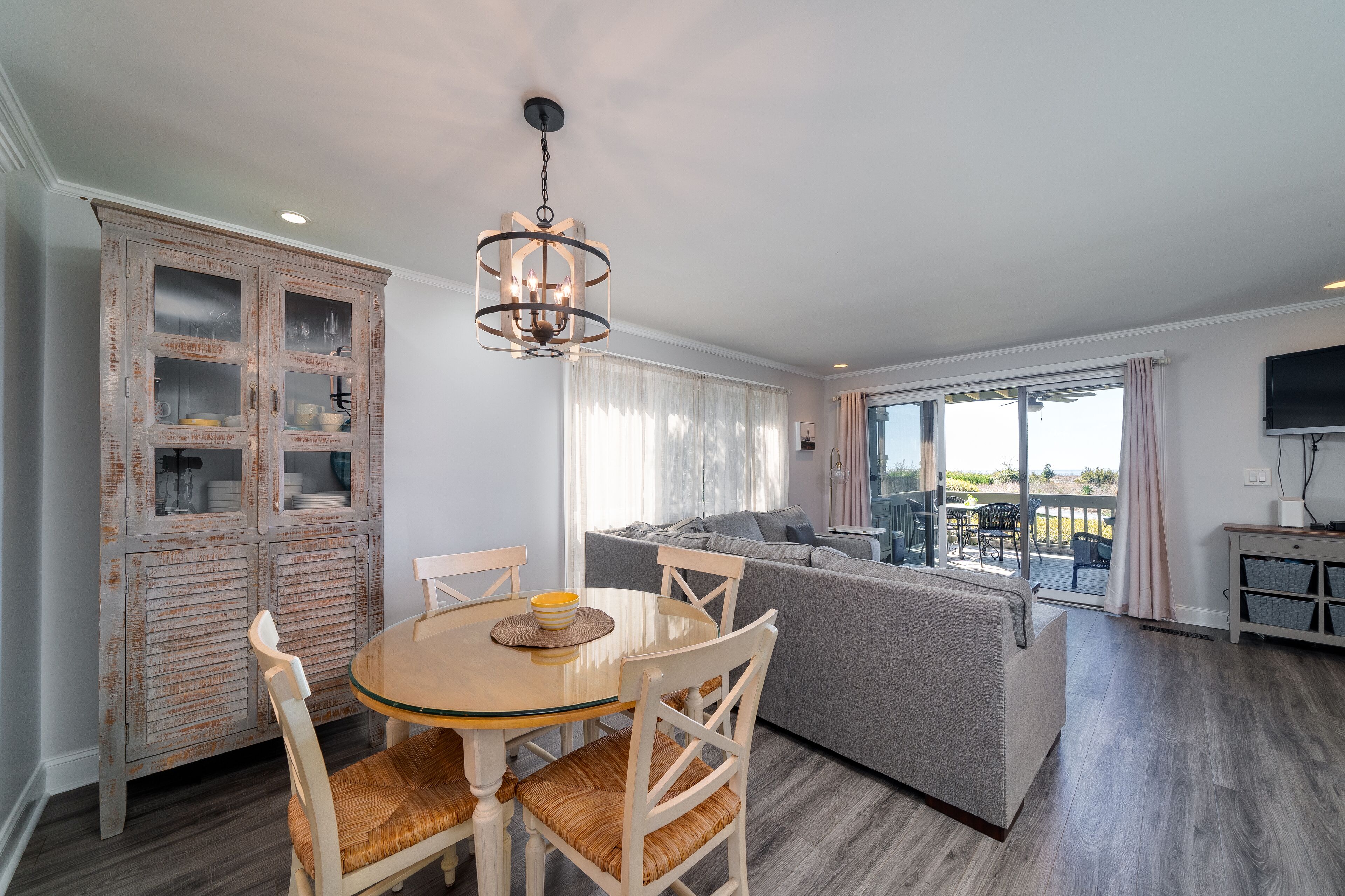 A dining area with a round table and chairs, a cabinet with glass doors, a sofa, and a television on a stand.