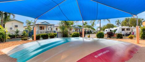 A covered outdoor area with a colorful surface, likely a pool or play area, surrounded by houses and RVs.
