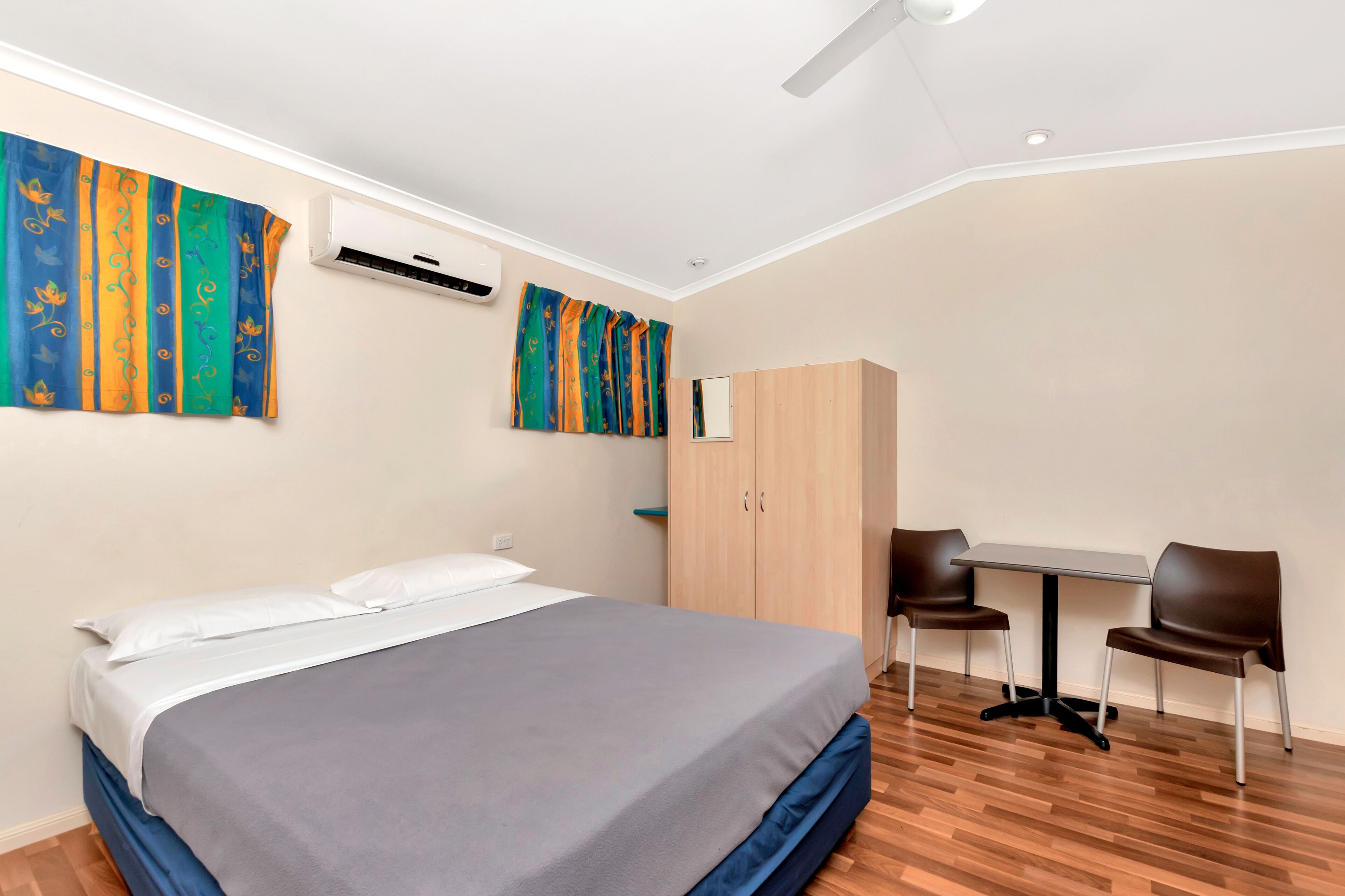 Un dormitorio con cama, escritorio, dos sillas, armario y equipo de aire acondicionado.