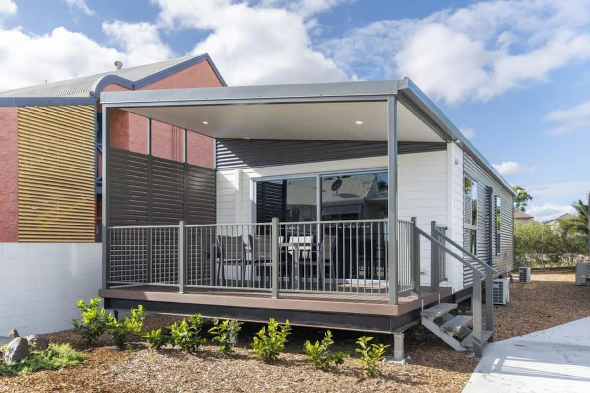 A modern mobile home with a covered patio, a fenced deck, and a small garden area.