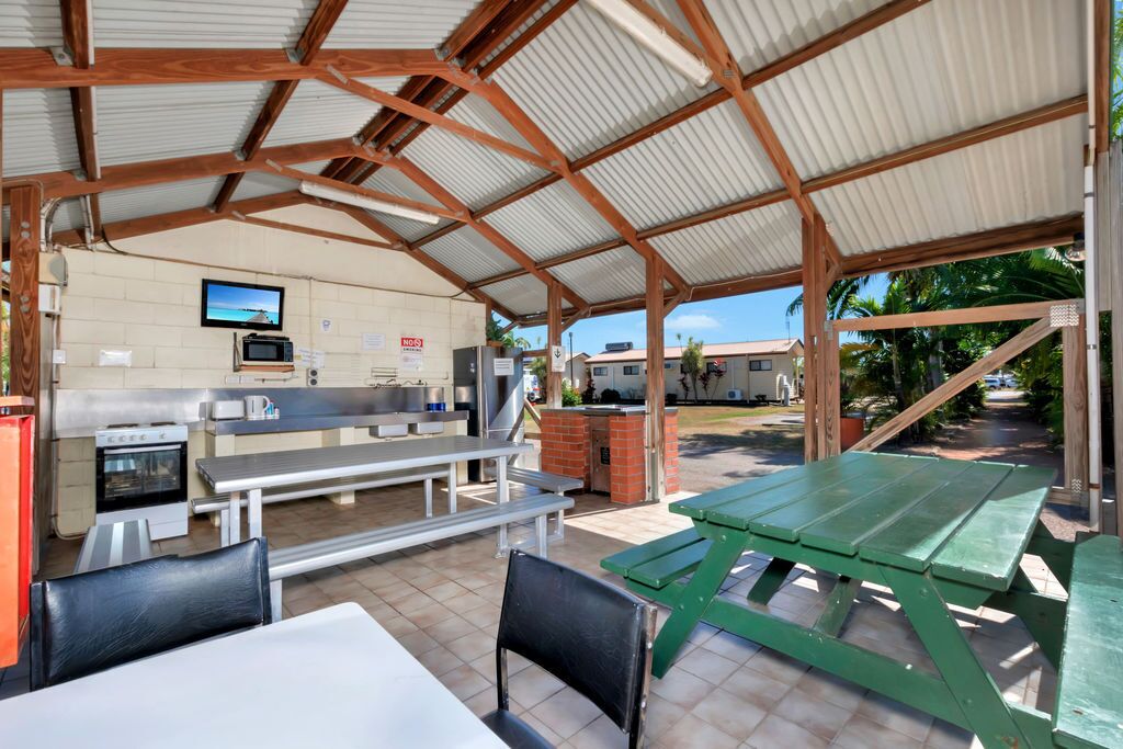 A covered outdoor dining area with picnic tables and benches, a kitchen area with a microwave, and a television mounted on the wall.