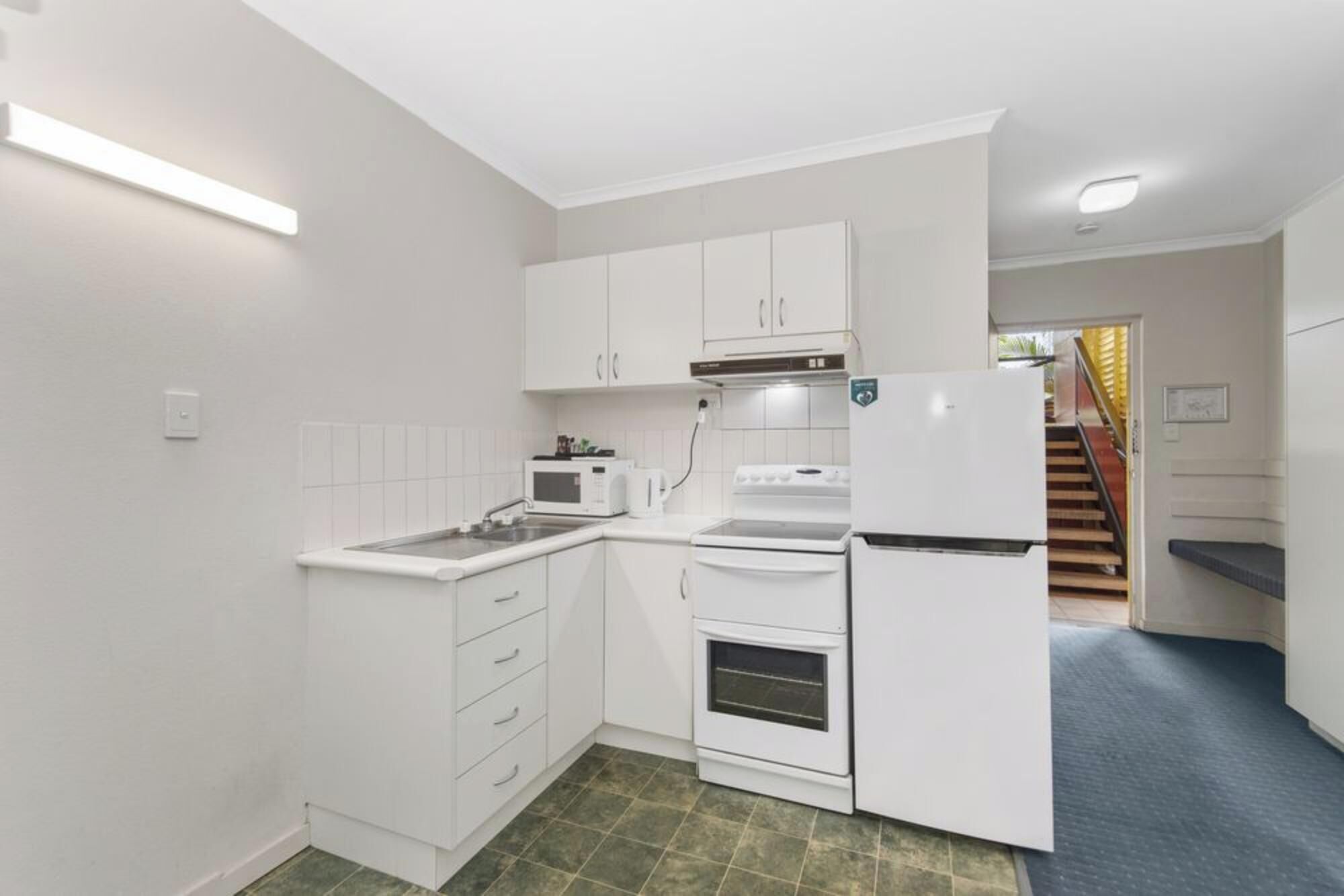 A compact kitchen with white cabinets, a microwave, stove, and refrigerator.