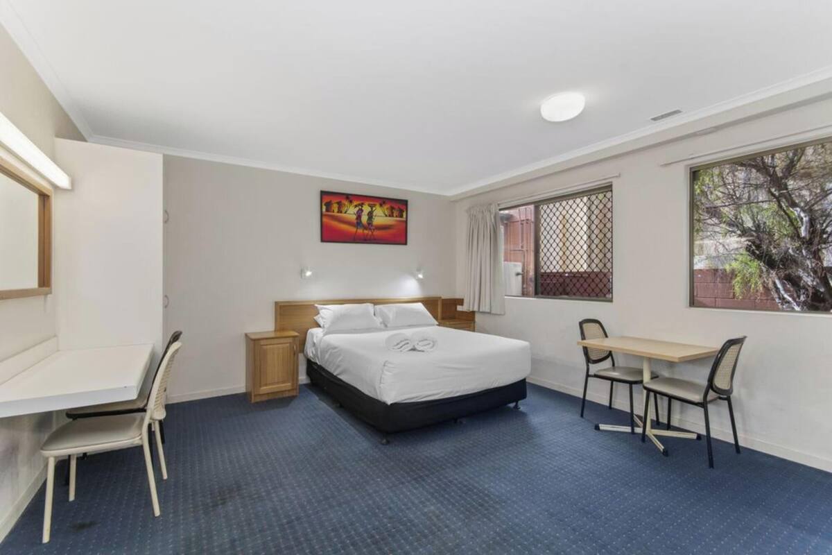 A hotel room with a bed, a desk, a chair, and a window.