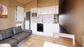 A compact living space with a sofa, a dining table, a kitchen area with cabinets and appliances, and a painting on the wall. - Discovery Parks - Townsville (Wulguru)