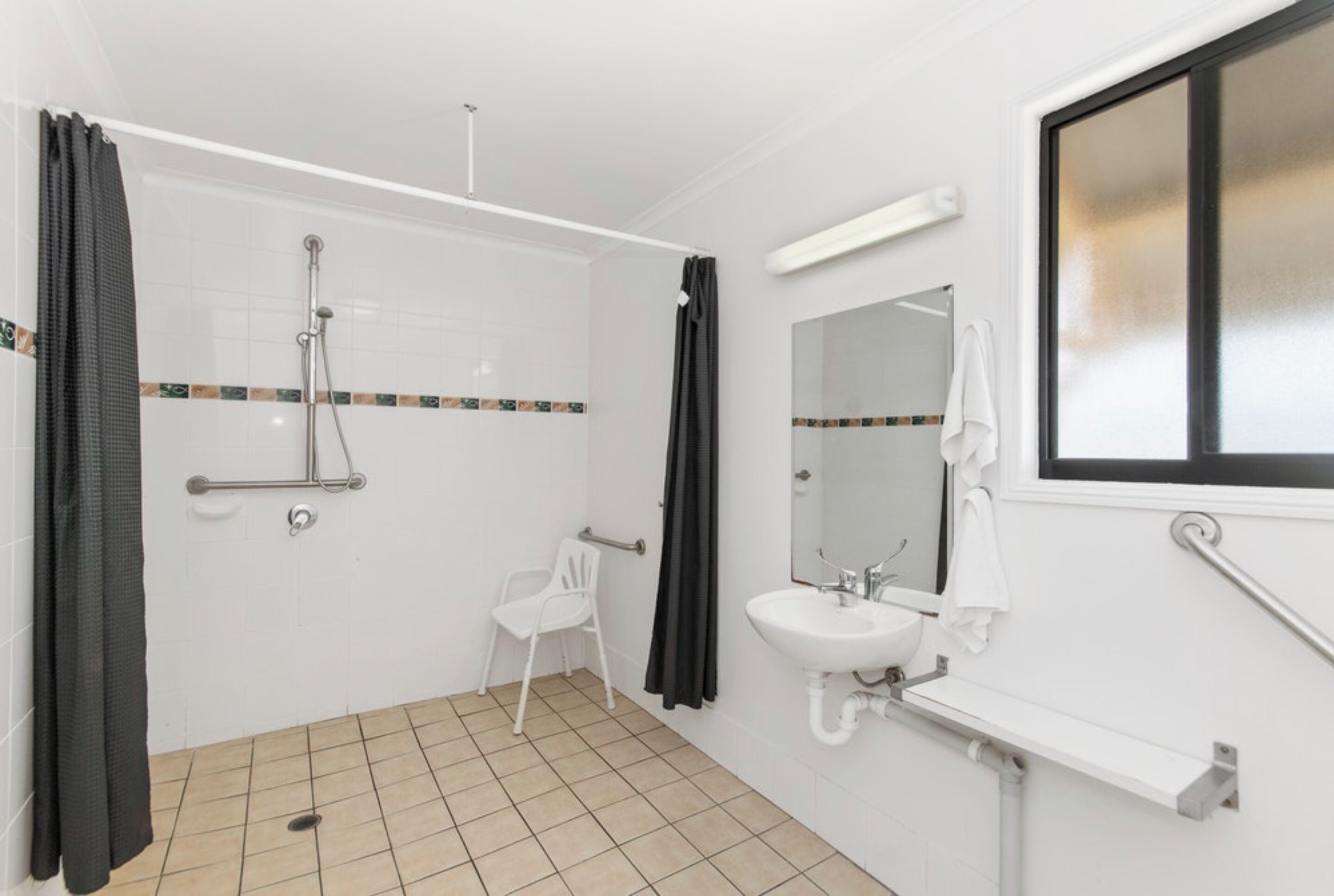 A bathroom with a shower, a sink, a mirror, and a chair.