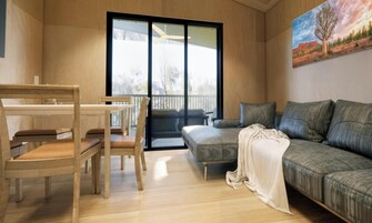 A modern living room with a wooden dining table, chairs, a sofa, and a large window.