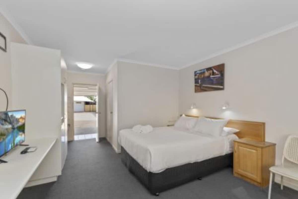 A bedroom with a bed, bedside table, lamp, and a desk with a computer.