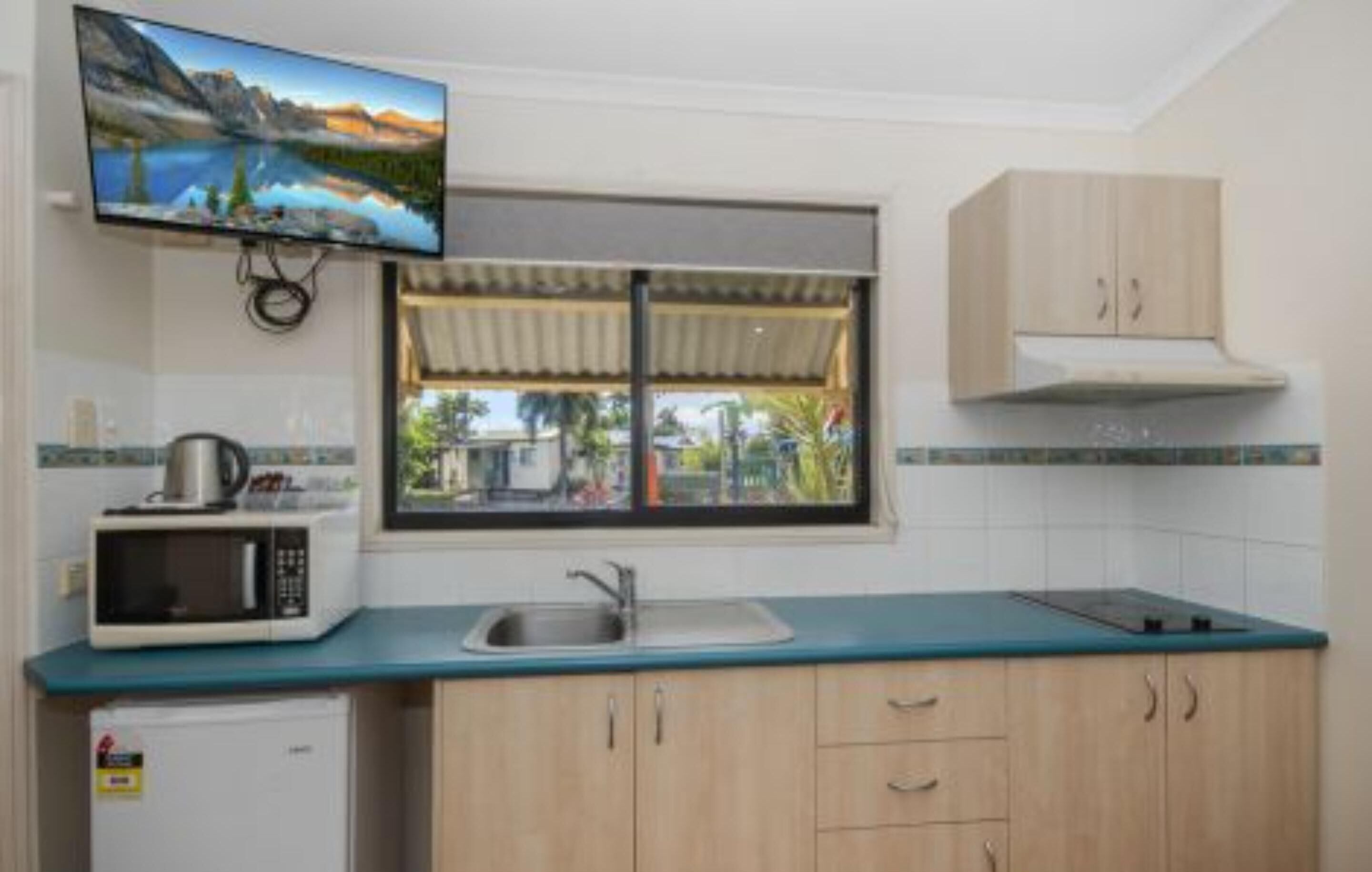 Cocina compacta con microondas, lavamanos y armarios de madera. Un televisor está montado sobre la ventana, la cual ofrece vistas a un paisaje montañoso.