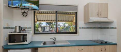 Cocina compacta con microondas, lavamanos y armarios de madera. Un televisor está montado sobre la ventana, la cual ofrece vistas a un paisaje montañoso.