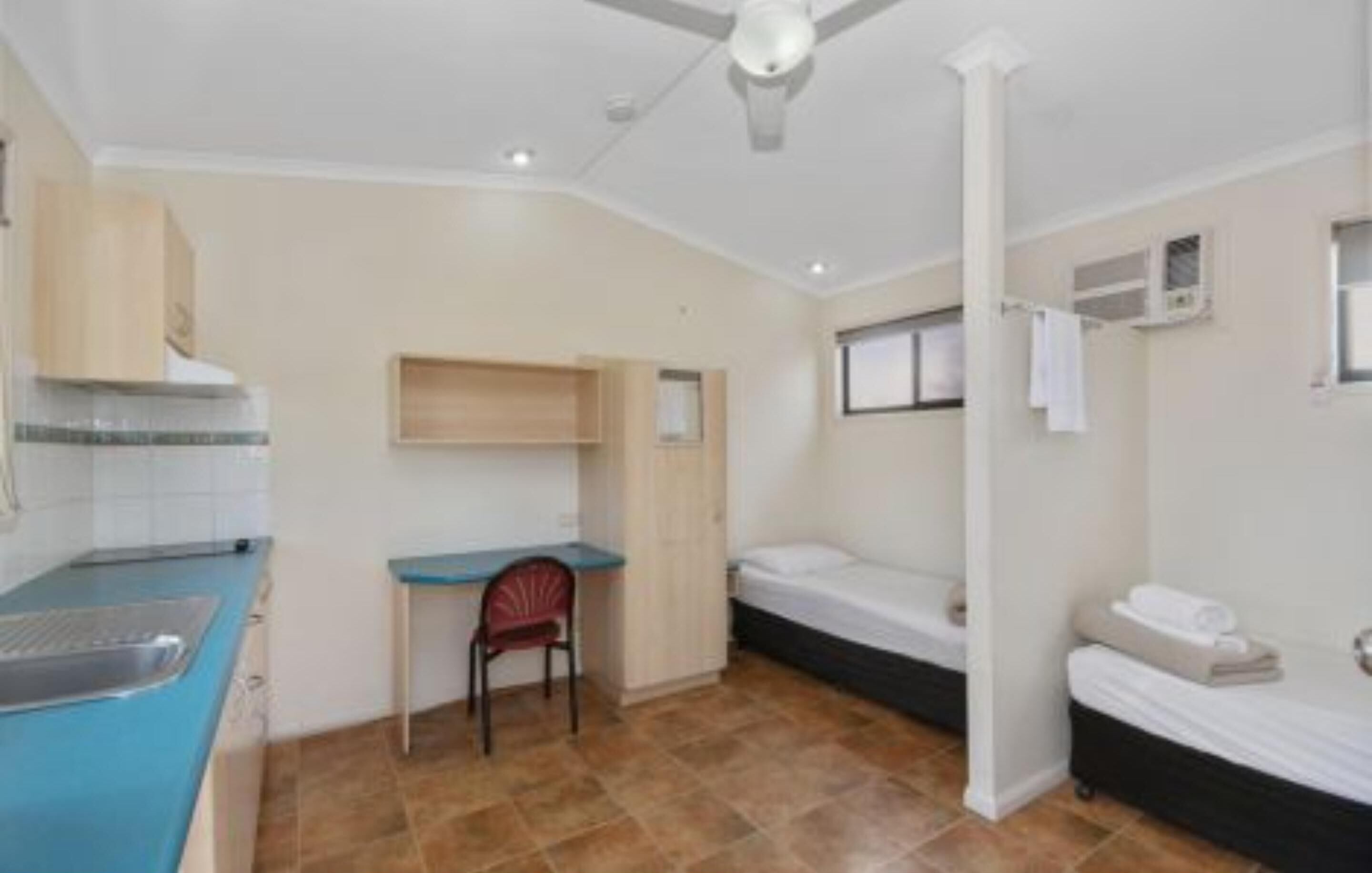A compact room with a kitchenette, a single bed, a desk, and a chair.