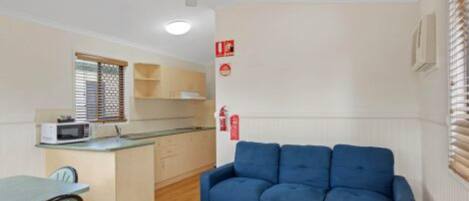 Un espacio habitable compacto con kitchenette, comedor y un sofá azul.