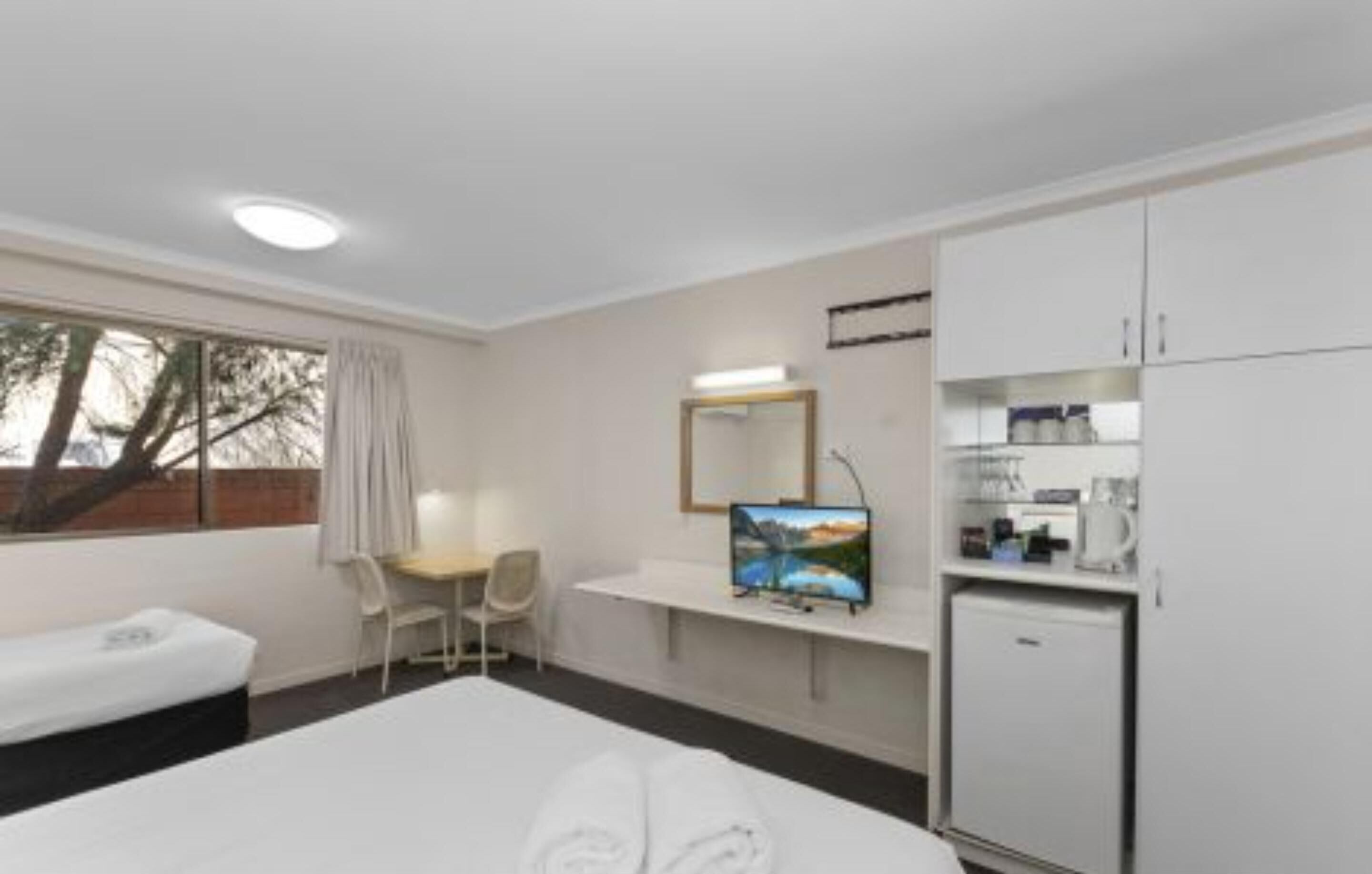 A hotel room with a bed, a desk, a television, a refrigerator, and a window with curtains.