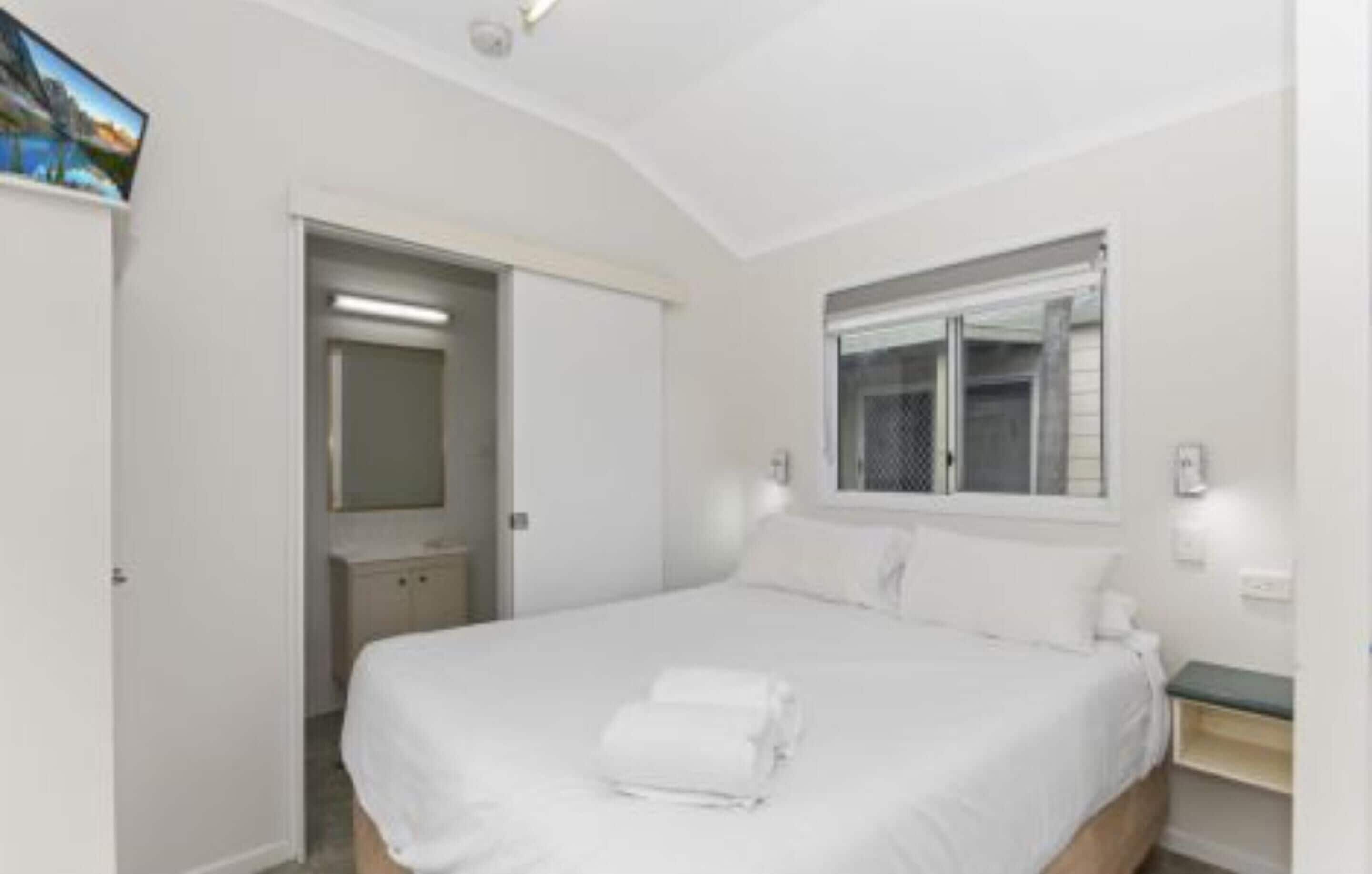 A bedroom with a bed, a nightstand, a mirror, and a window.