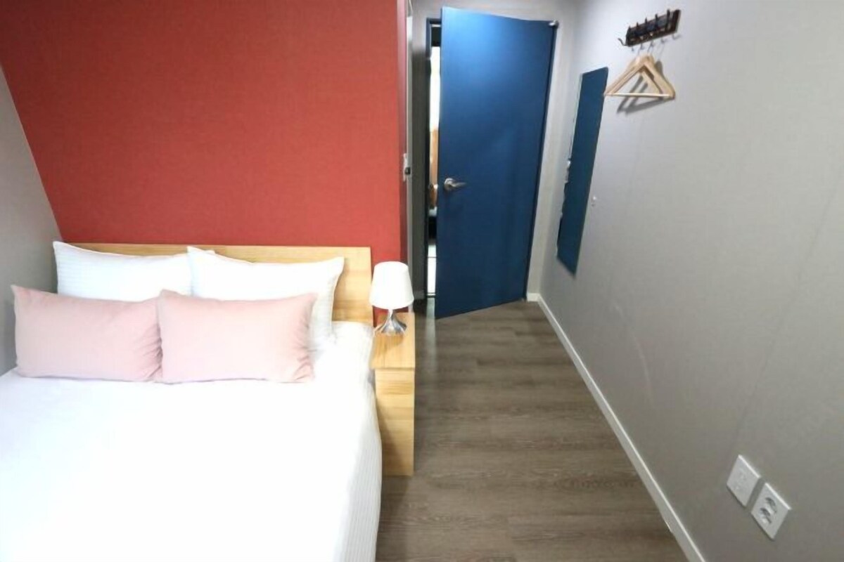 A hotel room with a bed, a nightstand, a lamp, and a door leading to another room.