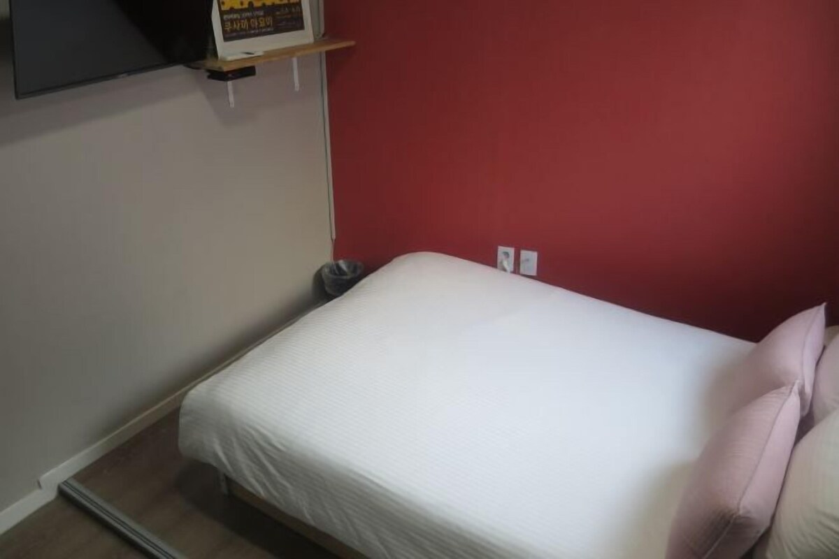 A small, single-bed room with a red wall, a white bedspread, and two pillows.