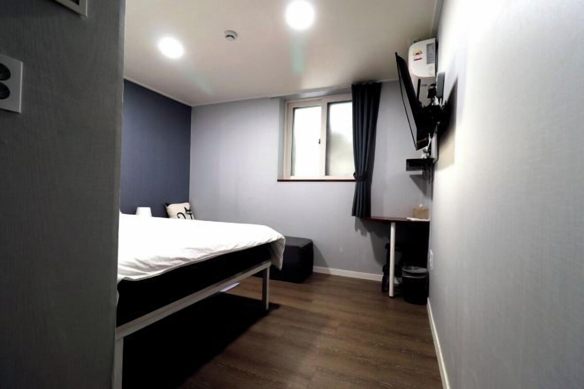 A bedroom with a bed, a desk, a chair, a window, and a ceiling light.