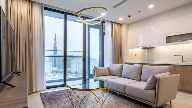 A modern living room with a sofa, a glass coffee table, and a view of a cityscape through large windows. - Vinhomes Central Park - MM Home (Ho Chi Minh City)